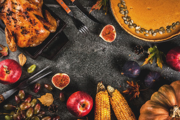 Thanksgiving Day food. Roasted whole chicken or turkey with autumn vegetables and fruits: corn, pumpkin, pumpkin pie, figs, apples, on dark grey background, top view