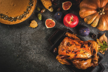 Thanksgiving Day food. Roasted whole chicken or turkey with autumn vegetables and fruits: corn, pumpkin, pumpkin pie, figs, apples, on dark grey background, top view  copy space