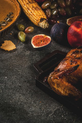 Thanksgiving Day food. Roasted whole chicken or turkey with autumn vegetables and fruits: corn, pumpkin, pumpkin pie, figs, apples, on dark grey background, copy space