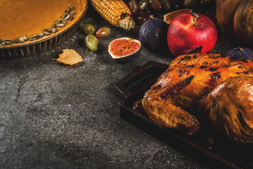 Thanksgiving Day food. Roasted whole chicken or turkey with autumn vegetables and fruits: corn, pumpkin, pumpkin pie, figs, apples, on dark grey background, copy space
