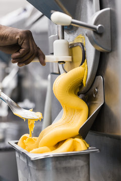 Thick orange mango ice cream pouring out from industrial machine