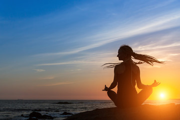 Fototapeta premium Yoga woman silhouette on the sea beach during sunset.