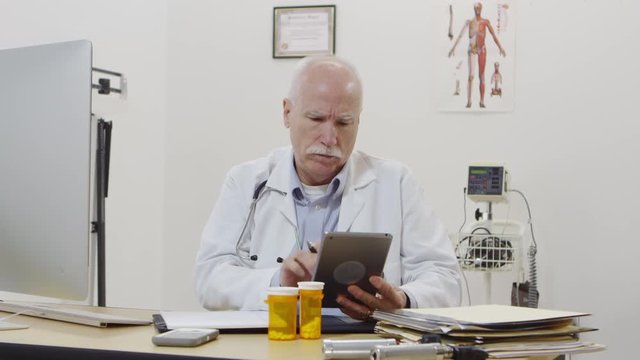 Elderly doctor using tablet and writing notes