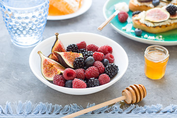 Fresh ripe summer berries and figs in the bowl with honey. Breakfast concept close up.