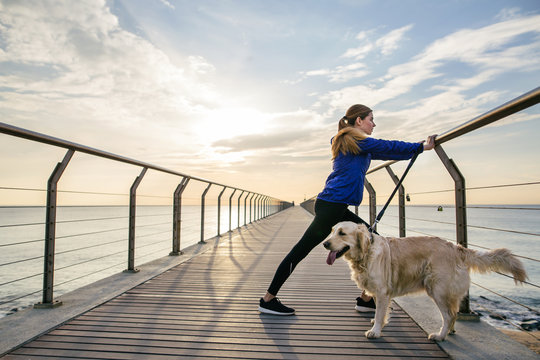 Woman doing stretching exercises with her dog on the bridge.