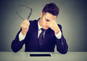 Frustrated man looking exhausted feeling tired sitting at his working place and carrying his glasses in hand