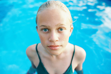 blonde teen girl with short hair slicked back in green one piece in swimming pool