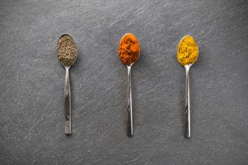 Drei L&ouml;ffel auf Schieferplatte nebeneinander, mit Paprika, Curry, Oregano