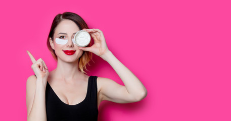 Woman using eye patch for her eyes and cream on pink background