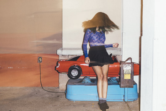 Woman fashion model posing and riding coin operated car ride at night
