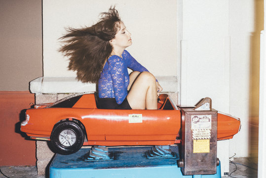 Woman fashion model posing and riding coin operated car ride at night