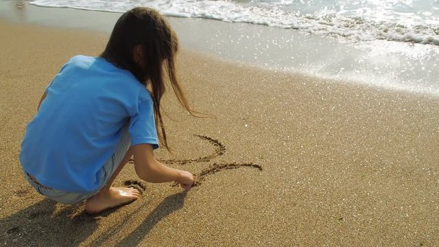 A little girl is writing on sand in 2018. A child writes 2018 on wet sand.