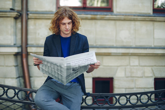 Young reddish man reading newspaper near old style building