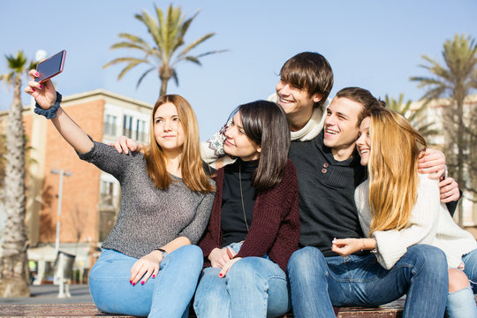 Group of teen friends taking a selfie with their phone outside.