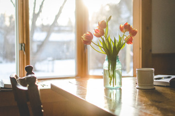 Tulips, coffee mug, and notebook on a table in a sunny, bright room