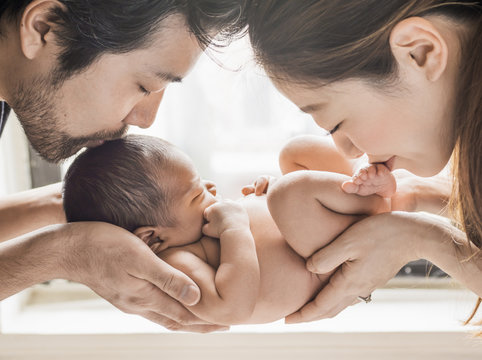 Happy new family portrait: Parents kissing a newborn baby