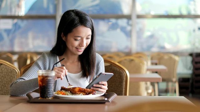 Woman using cellphone and having lunch in restaurant