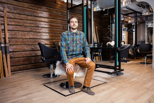 Confident Male Hairdresser Sitting On Chair At Beauty Salon