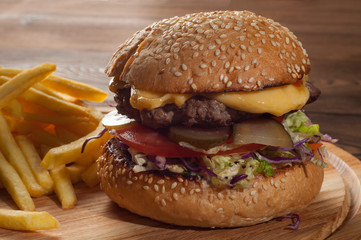 Big burger with french fries close-up on a wooden cutting board