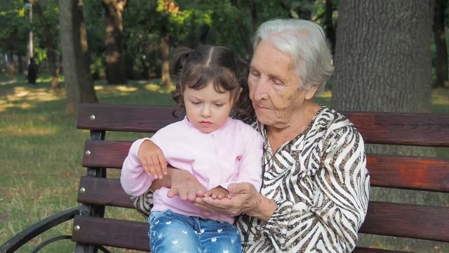 Granddaughter sits on the hands of his grandmother. An elderly woman with a little girl looks at her hands.
