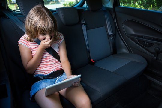 Teenage girl using digital tablet in the back seat of car