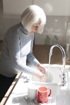 Senior Woman Doing The Dishes At The Kitchen Sink