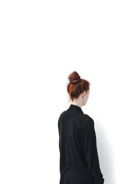 Stark anonymous image of the back of a red headed woman and white wall