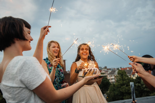 Young women having fun on a rooftop with sparklers and birthday cake.