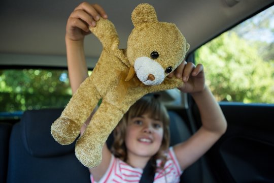 Teenage girl playing with teddy bear in back seat of car