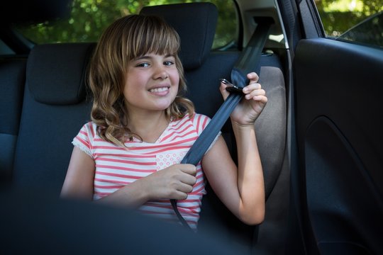 Happy Teenage girl wearing seat belt in the back seat of car