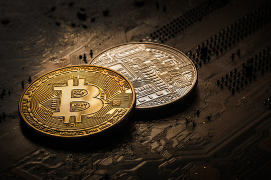 Gold and silver bitcoin on a dark background of a computer board.