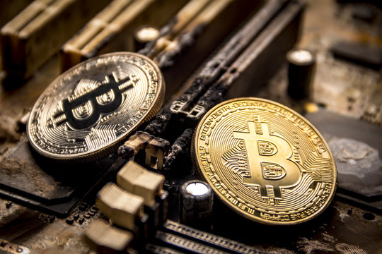 Gold and silver bitcoins on the background of a burnt electronic computer board.