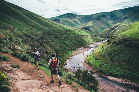 fly fishermen hikers walking on a mountain path overlooking a valley and river