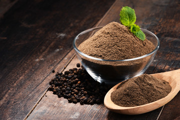 Composition with bowl of ground black pepper on wooden table