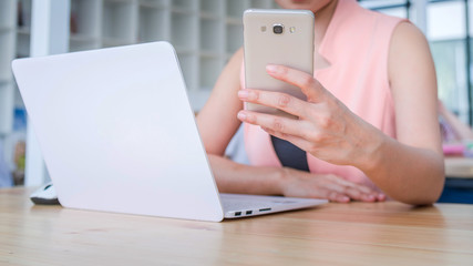 female hands using phones and working with a laptop in office at desk