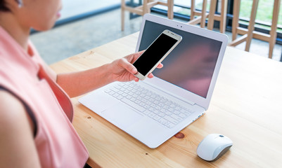 female hands using smart phones and working with a laptop in office at wooden desk