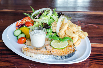 Fish steak, grilled salmon and fresh vegetable salad, french fries and sauce on a white plate