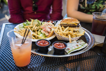 Food, lobster roll, salad, ketchup, relish and burger with fries, and drinks with two people sitting in New York City