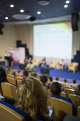 Business and Entrepreneurship Ideas. Female Speaker On Stage Giving a Talk at Business Meeting or Conference. Back View of the Listeners.