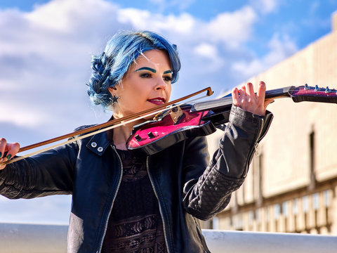 Woman perform music on violin in park outdoor. Girl performing jazz on city street. Spring outside with blue hairstyle background. Street musician makes money for a living.