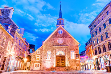 Obraz premium Dolna ulica starego miasta w Quebec City w Kanadzie na La Place Royale o zmierzchu, w nocy lub o zmierzchu z kościołem Notre-dame-des-Victories i ludźmi z wieczornymi światłami