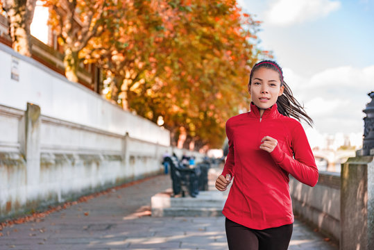 Woman running in autumn fall outdoor city street. Female runner training outdoor in profile. Healthy lifestyle image of young Asian woman jogging outside. Fit ethnic Asian Caucasian fitness model.