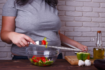 Dieting, healthy low calorie food, weight losing concept. Overweight woman with measuring tape on her waist eating salad from a bowl