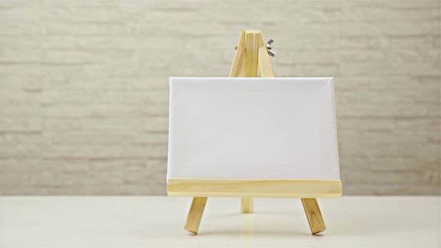 Empty canvas on mini easel alone on table slide from right to left 4K