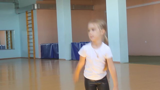 A beautiful girl is engaged in dancing in the dance hall. The child looks at the reflection and performs the exercises. Dancing school.
