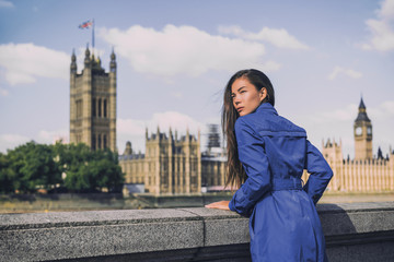 London city Europe travel destination Asian woman at Westminster Houses of Parliament. Autumn holiday tourist wearing blue rain coat for fall. Urban lifestyle.