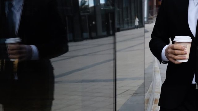 Businessman talking on mobile cell phone in city wearing suit in city business district. Talking on smartphone. Urban male drinking coffee. Middle Slow motion shot.