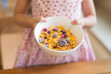 Morning breakfast, little girl hand holding cornflakes cereal, strawberry, blackberry and milk in a white bowl