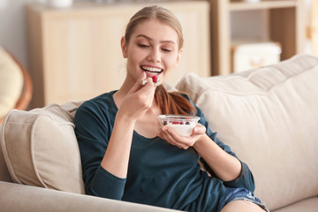 Young woman eating yogurt on sofa at home