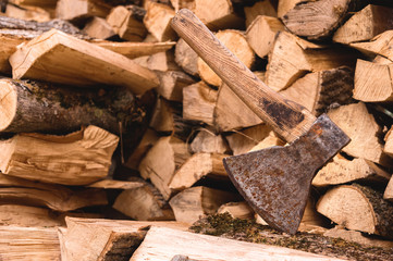 The ax is stuck in a log against the backdrop of chopped firewood lying in a flat pile